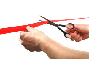 Scissors cutting through red ribbon or tape, isolated on white. Scissors cutting ceremony